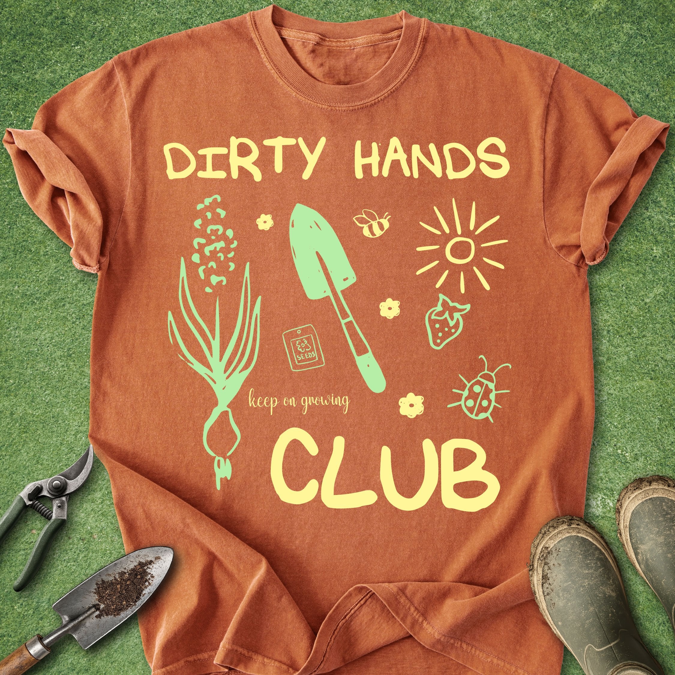 Brown t-shirt with gardening-themed graphics and text on a green grass background